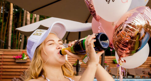 girl drinking champagne from a bottle, balloons in the background