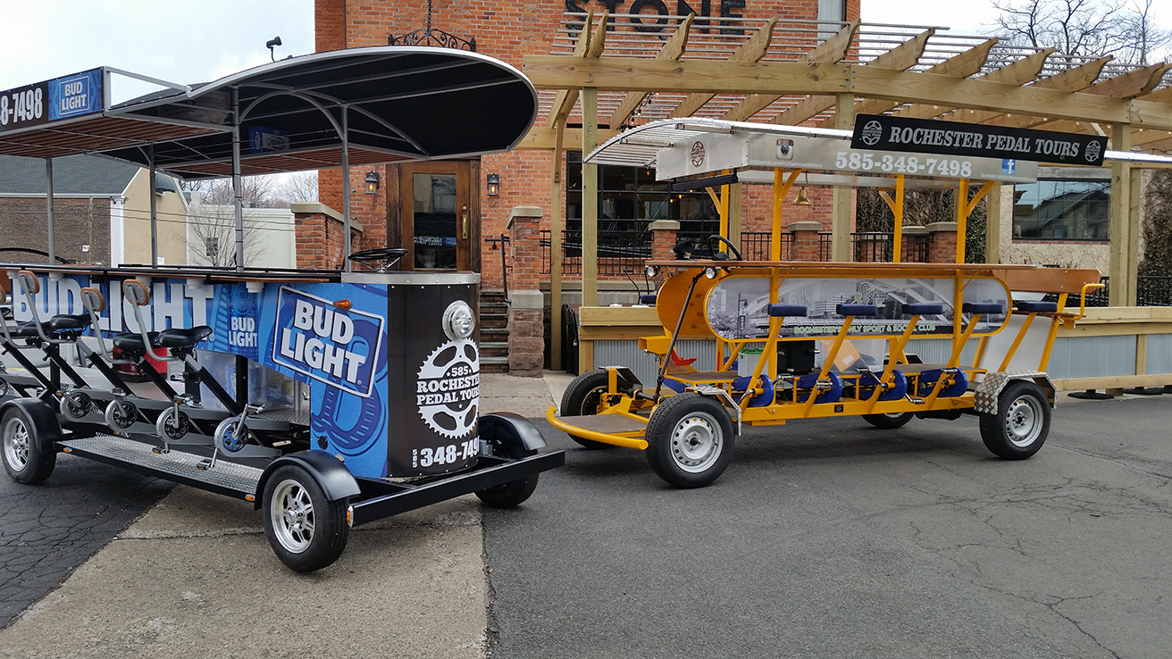 two pedal pub bikes one orange and one blue parked in front of a brick made building