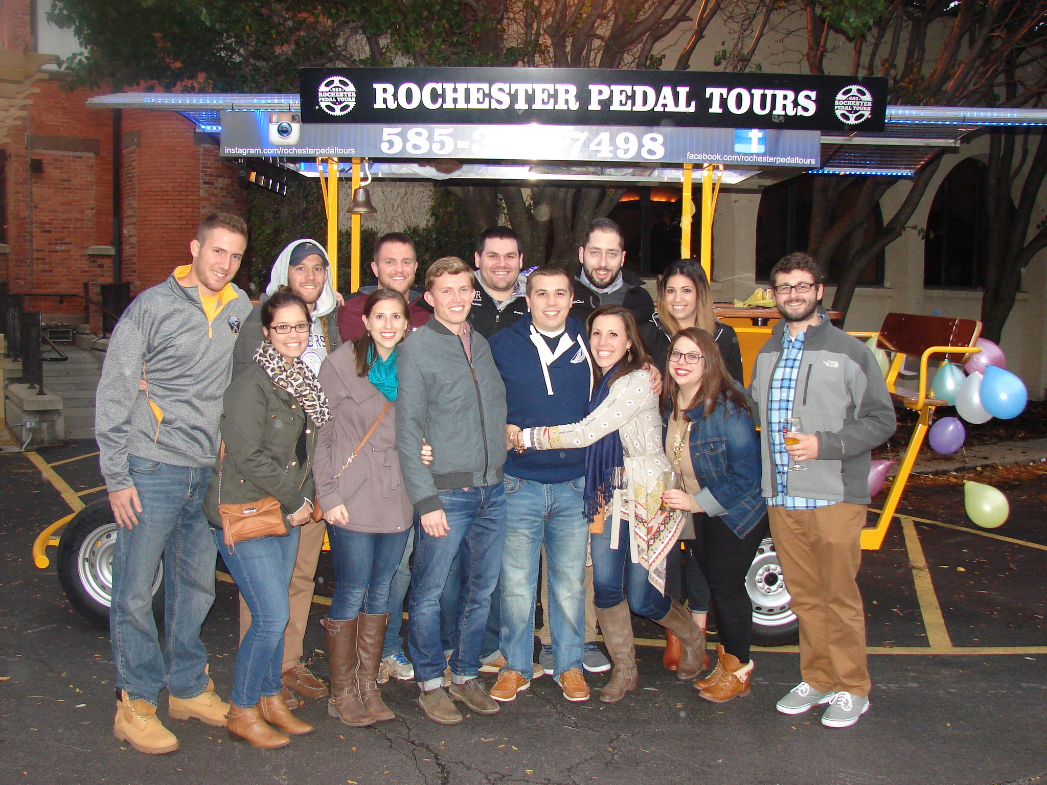 group of people with wide smiles posing for a picture in front of a pedal pub