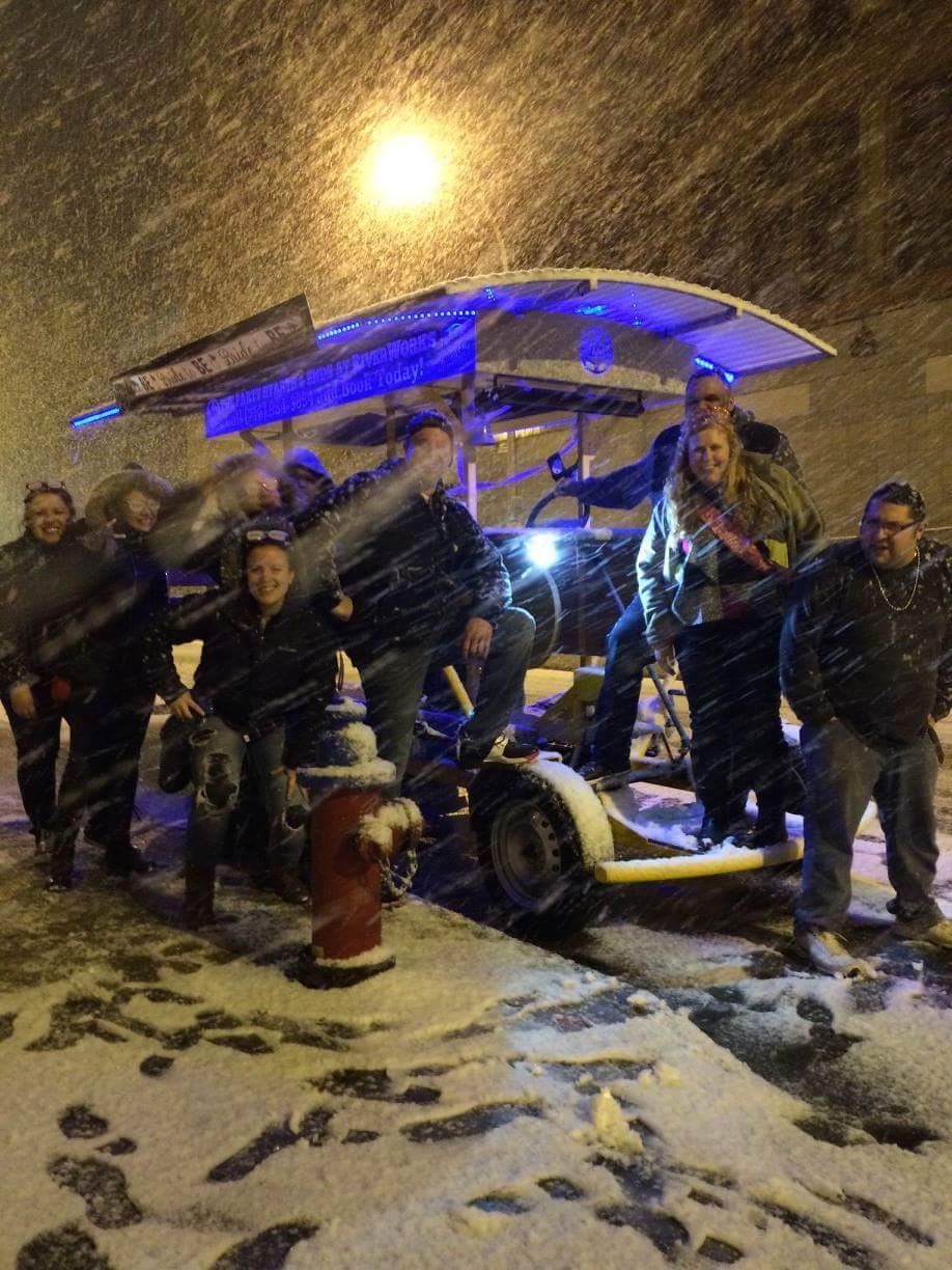 group of people smiling and posing on a pedal pub while being in the heavy snow
