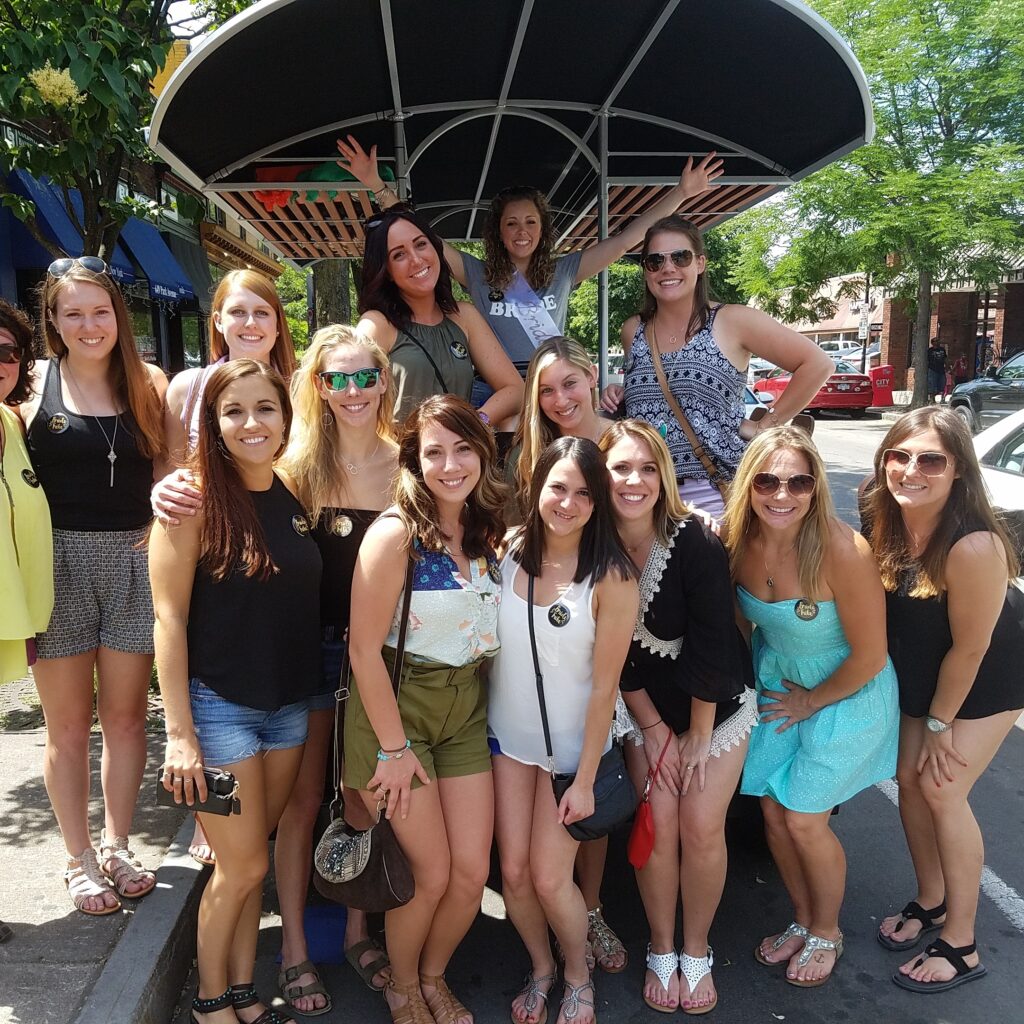 group of ladies in the summer posing for a picture in front of a pedal pub in the city