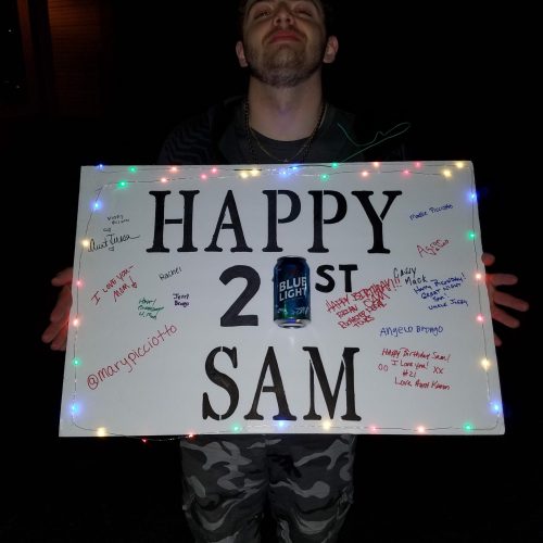 guy with a smirk on his face posing for a picture holding a sign indicating a 21st birthday