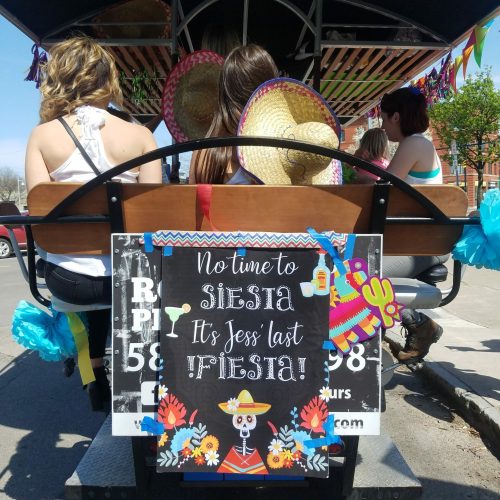group of ladies riding a pedal pub that is decorated with signs trough the city