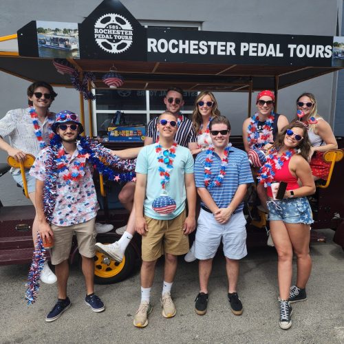 Group of people posing for a picture in front on pedal pub wearing sunglasses on 4th of July