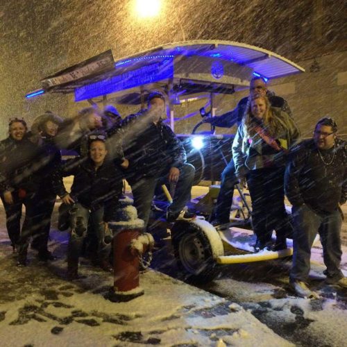 group of people smiling and posing on a pedal pub while being in the heavy snow