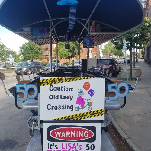 pedal pub parked in a city having a sign on it that is displaying a 50th birthday celebration