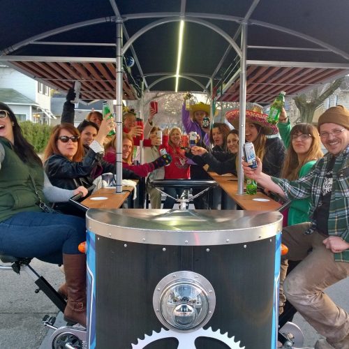 group of people sitting o na pedal pub having drinks and posing for a picture